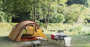 自然の中に設営されたテントとキャンプ用品が並ぶ静かなキャンプサイトの風景 