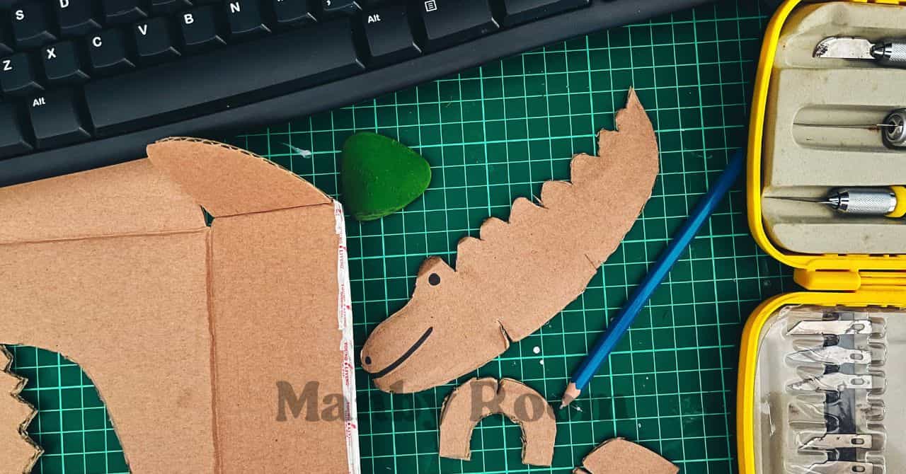 段ボールで作られたワニの顔やパーツと道具。ごっこ遊びや工作を楽しむ4〜6歳向けのシーン。