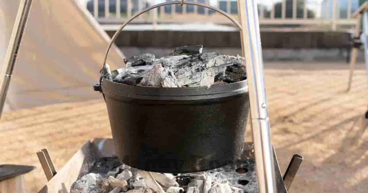 炭火で調理中のダッチオーブンに炭が乗せられたキャンプ飯の準備風景