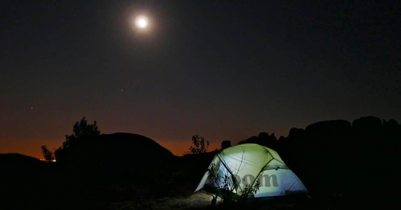 夜空に月が輝く中、冷え込む空気のなかで静かに灯るテント。就寝時の寒さ対策の大切さを伝えるシーン。
