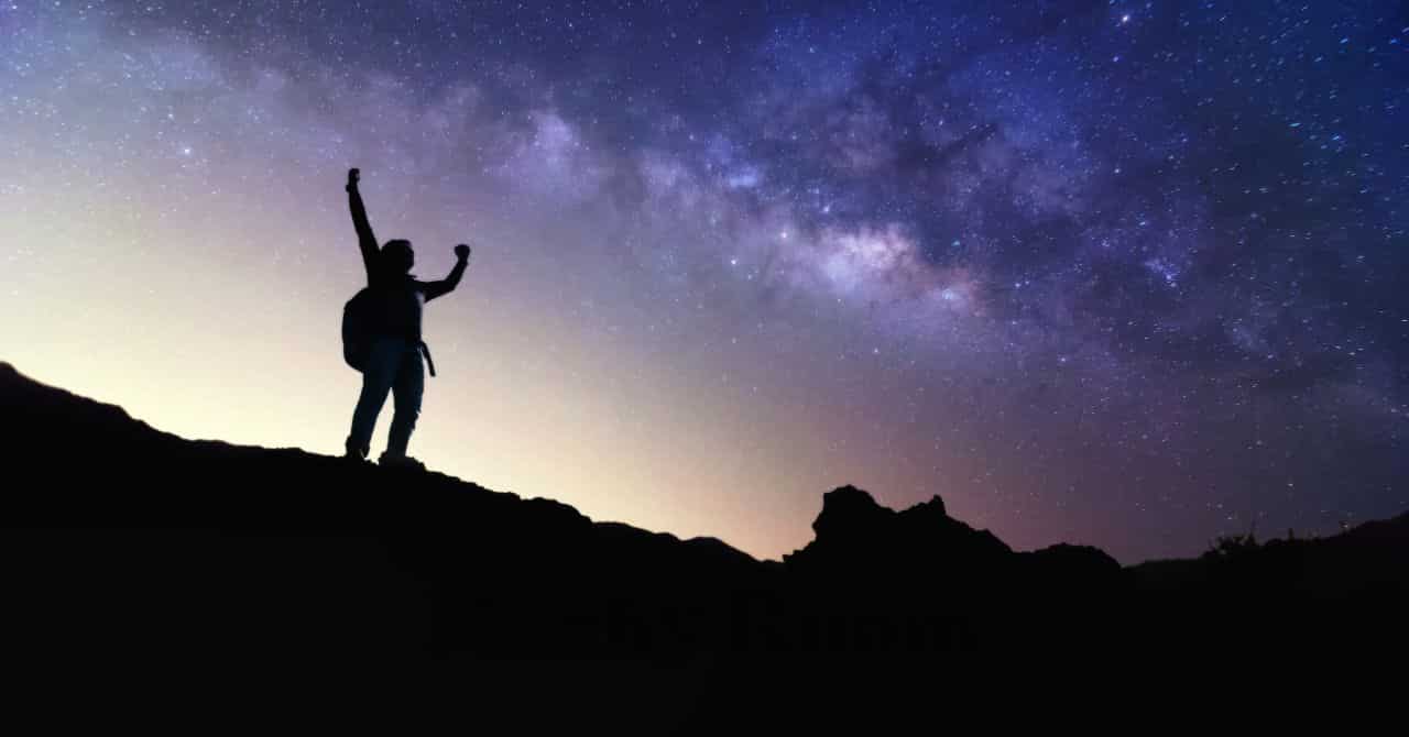 満天の星空の下、両手を上げて立つ人のシルエット。夜のキャンプ時間を特別な体験として楽しむことを象徴する一枚。
