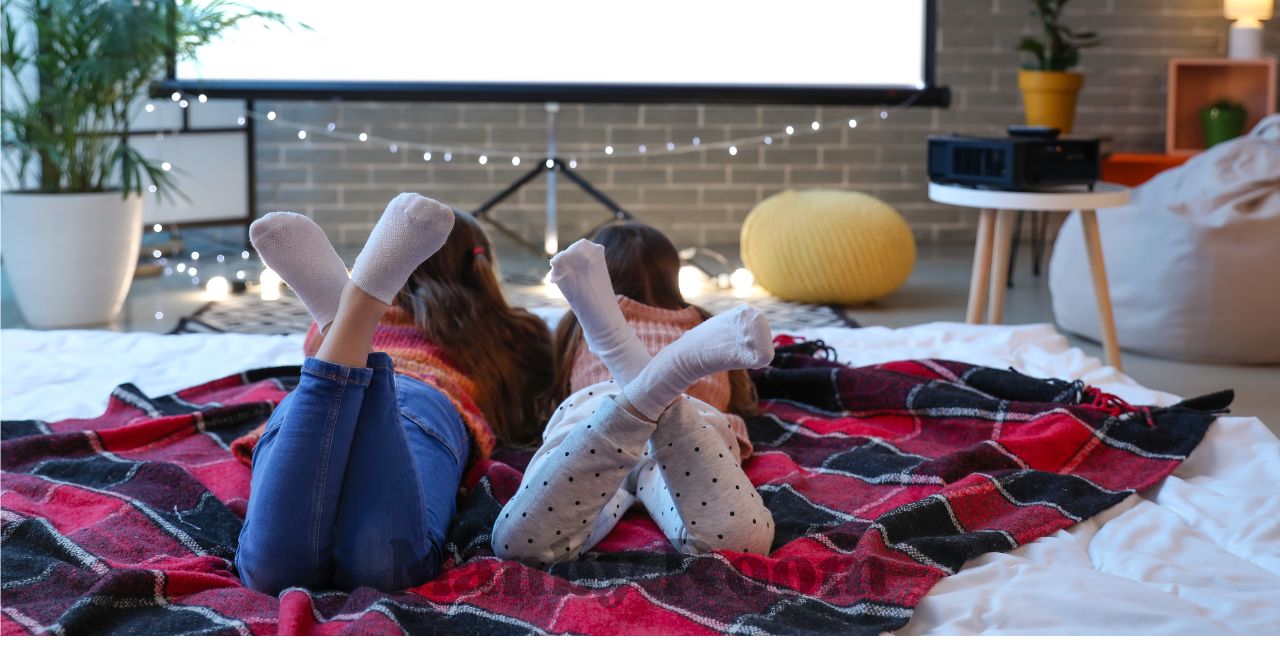 毛布にくるまりながらおうち映画を楽しむ親子の後ろ姿
