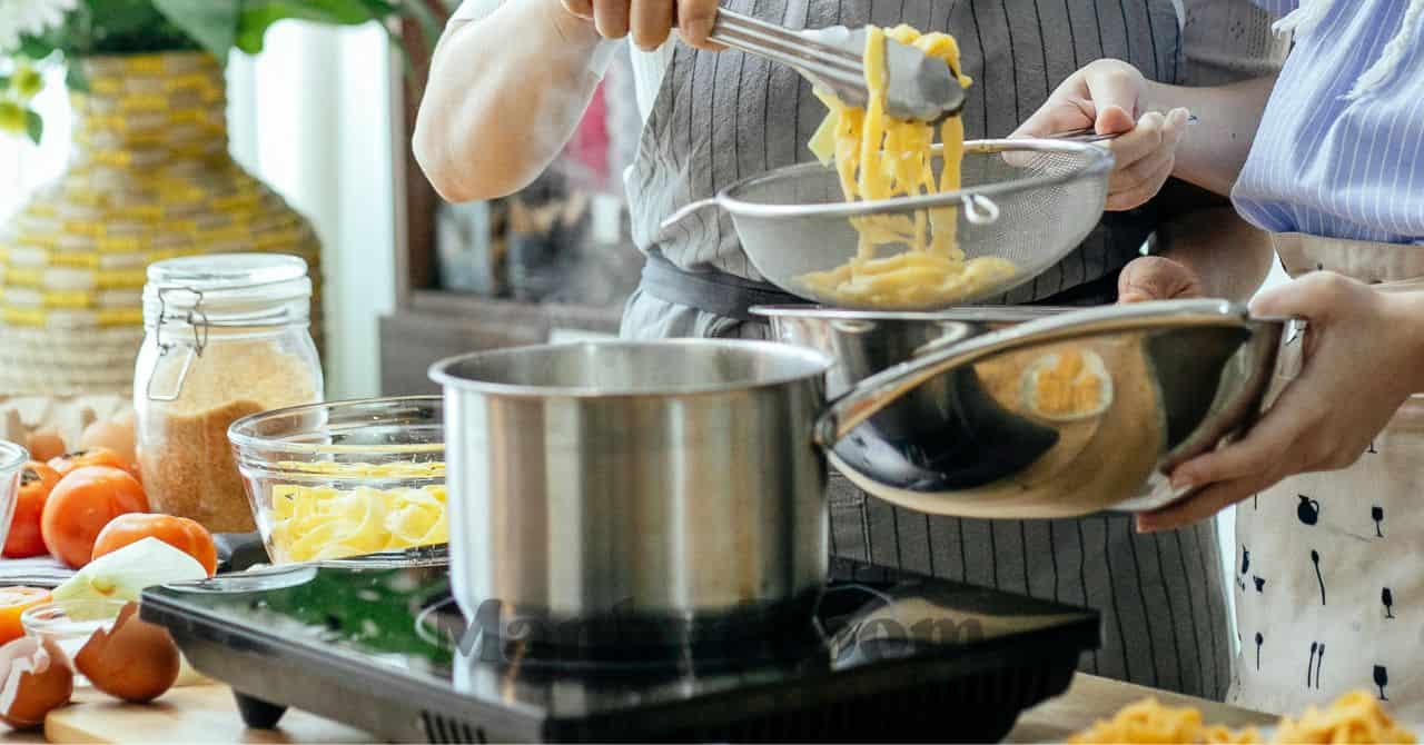 親子が協力して茹で上がったパスタをざるに移し、ボウルに分けている様子
